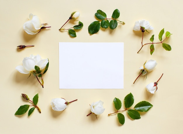 Flores e papel branco em uma vista superior de fundo amarelo claro