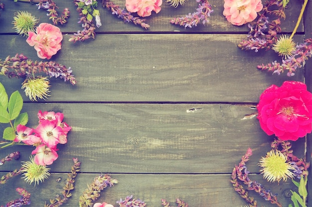 Flores em um círculo em um fundo de madeira Cartão postal para o feriado Rosas gerânios lavanda sálvia e castanhas peludas são colocadas ao longo das bordas em placas escuras Espaço de cópia de fundo plano lay