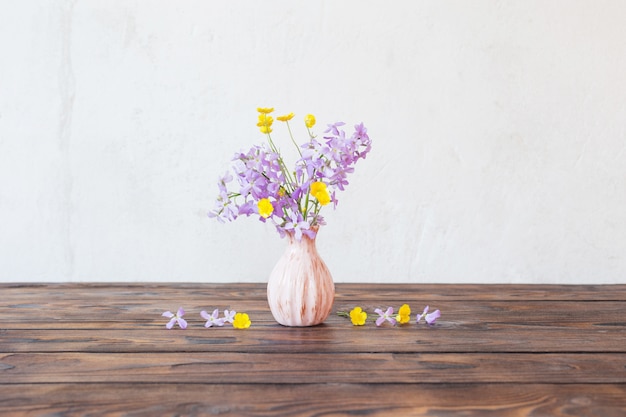 Flores en florero sobre mesa de madera en la pared de fondo blanco