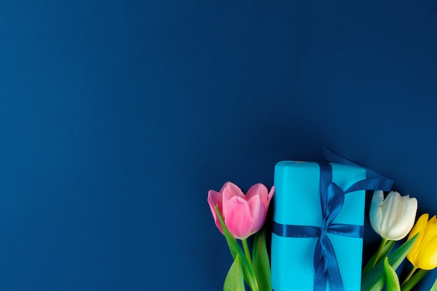 Flores frescas y caja de regalo con cinta sobre fondo azul clásico