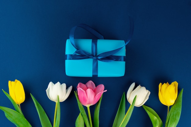 Flores frescas y caja de regalo con cinta sobre fondo azul clásico