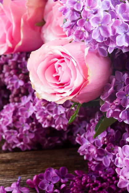 Flores frescas de color lila púrpura con rosas rosadas en la mesa de madera de cerca