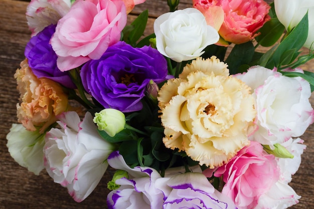 Flores frescas de eustoma rosa, branco, laranja e violeta em fundo de madeira envelhecido