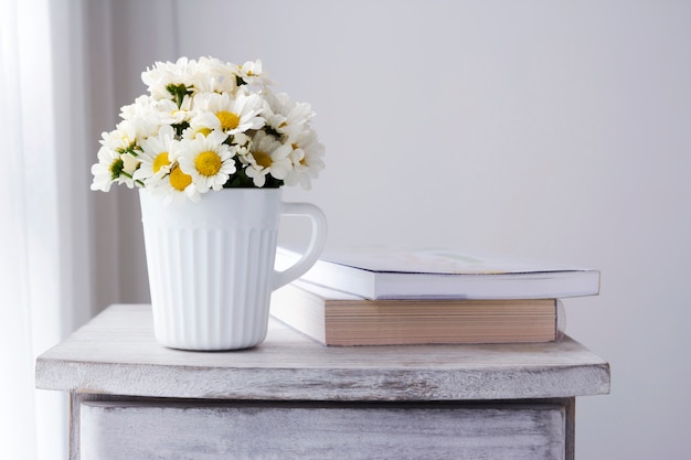 Flores frescas de la margarita en la taza blanca en el gabinete de madera