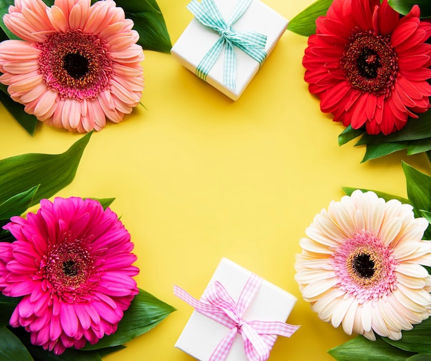 Foto flores gerbera e caixas de presente em uma mesa amarela. vista do topo