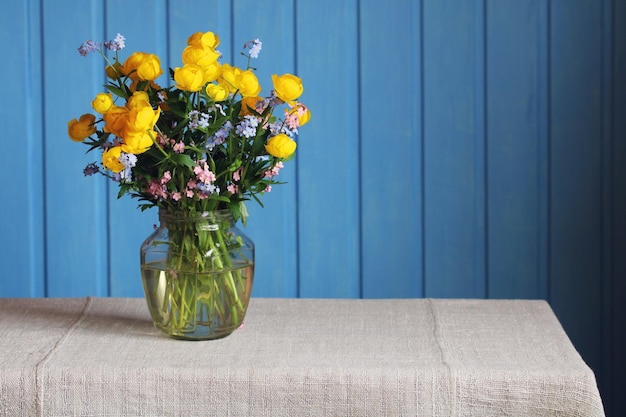 Flores globo amarelas e forgetmenots em uma jarra de vidro em um fundo azul lindo buquê de flores silvestres