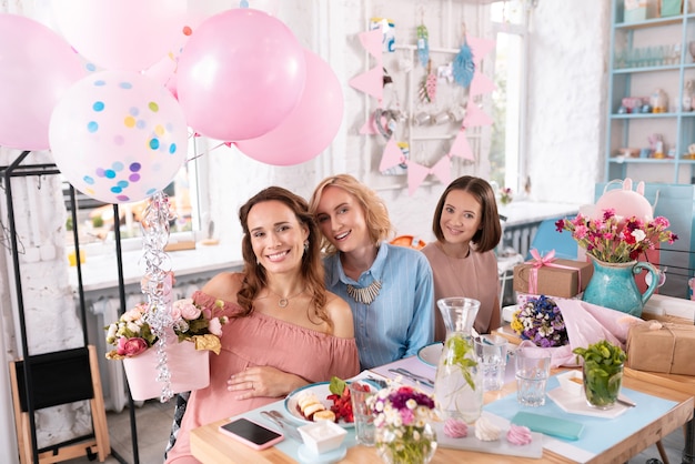 Flores y globos. Feliz mujer radiante que se siente alegre mientras sostiene bonitas flores decoradas con globos de aire