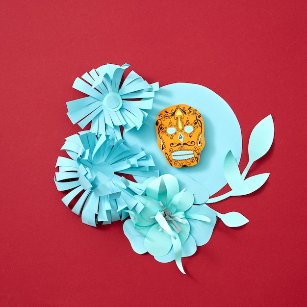 Foto flores y hojas de papel artesanales decoran el marco azul con el atributo calaveras de la fiesta mexicana de calaca sobre un fondo rojo con espacio para texto. postal creativa de halloween. endecha plana