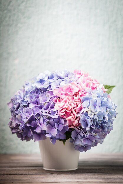 Flores de hortensia en el balde blanco sobre la mesa de madera