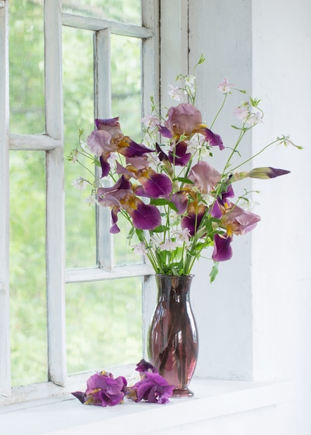 Flores de iris en jarrón de vidrio sobre blanco alféizar antiguo