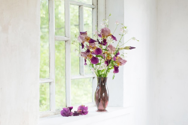 Flores de iris en un jarrón de vidrio sobre un viejo alféizar blanco