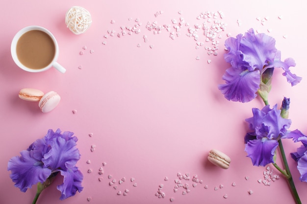 Flores de iris morado y una taza de café sobre un fondo rosa pastel.