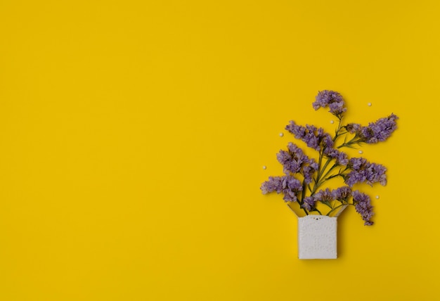 Flores de lavanda púrpura en caja blanca con perlas blancas sobre fondo amarillo