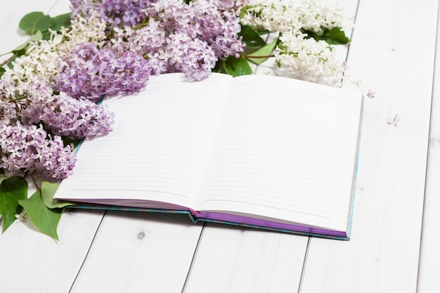 Flores lilas blancas y violetas abrieron un cuaderno vacío en una vista en perspectiva de fondo de madera blanca