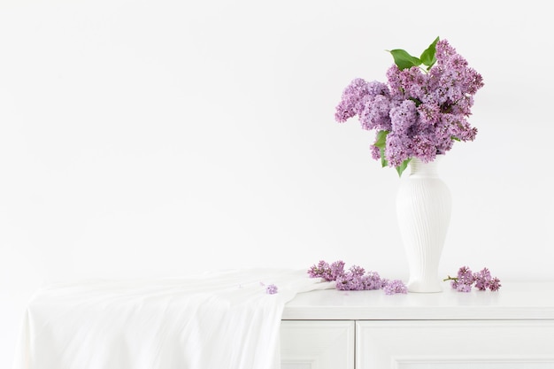 Flores lilás em vaso branco na parede branca de fundo