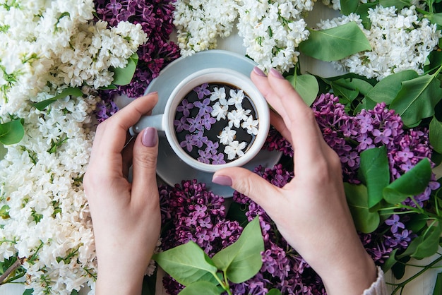 Flores lilas en una taza de café en las manos de una niña concepto de publicidad de cafetería