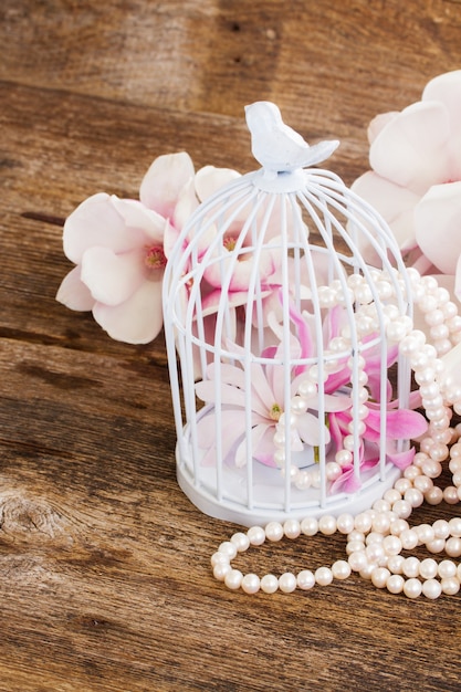 Flores de magnolia con perlas y jaula en mesa de madera