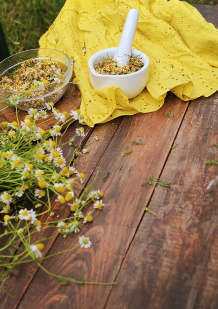 Flores de manzanilla orgánica en maja de porcelana de pie sobre una mesa de madera, concepto de tratamiento de la naturaleza