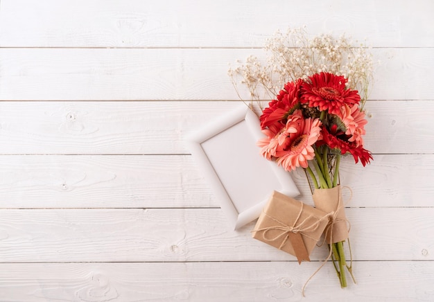 Flores de margarita de gerbera roja y caja de regalo artesanal de marco blanco con etiqueta en la mesa de madera blanca