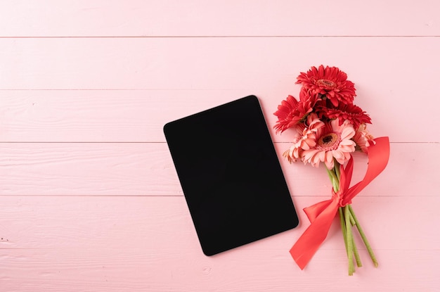 Flores de margarita de gerbera roja y tableta digital en mesa de madera rosa