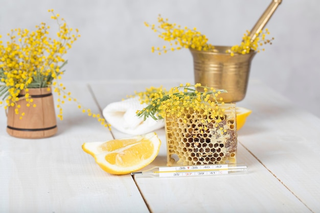 Flores de mimosa, panal, dos trozos de limón sobre una superficie de madera color leche.