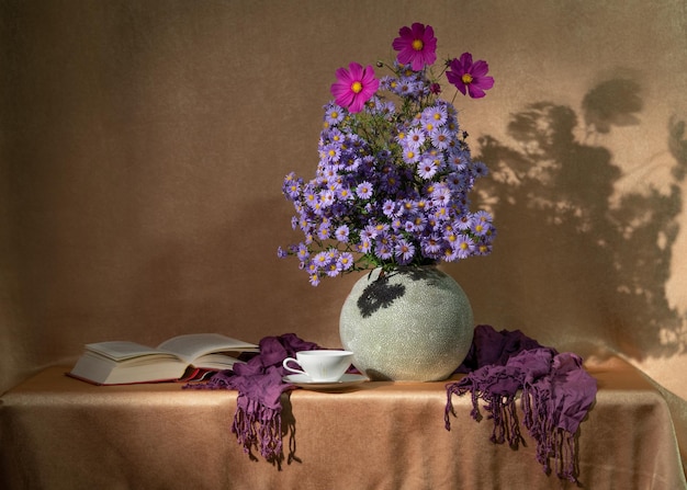 Flores moradas de verano en un jarrón y un libro con una taza sobre la mesa