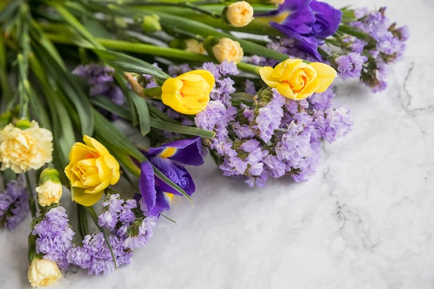 Flores de narciso amarillo y lirios púrpuras en un arreglo floral de línea aislado sobre fondo de mármol.