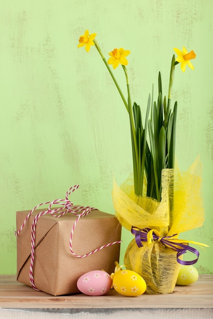 Flores de narciso, caja de regalo y huevos de pascua sobre fondo verde