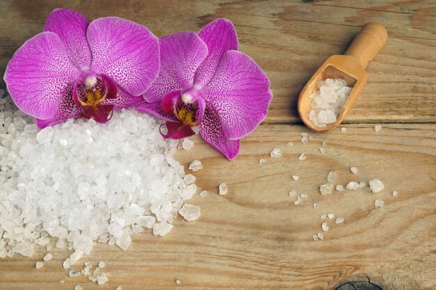 Flores de orquídea sobre un fondo de madera con sal marina blanca para el cuerpo