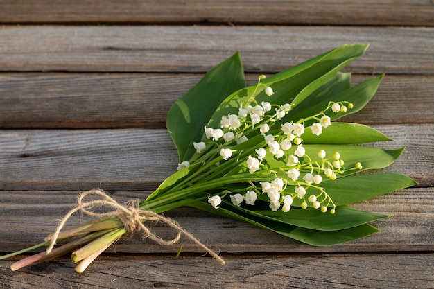 Flores parcialmente borrosas sobre una rústica superficie de madera vieja. Un ramo de lirios del valle en las tablas. Copie el espacio.