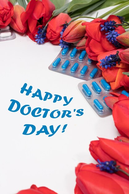 Flores y pastillas con inscripción Feliz día del médico en blanco.