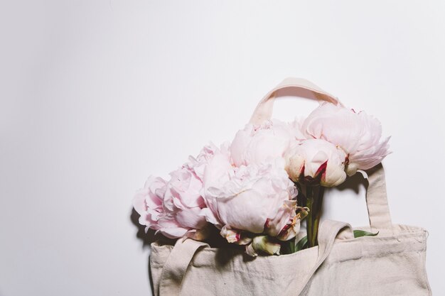 Flores de peonías rosas en la bolsa de algodón sobre fondo blanco.