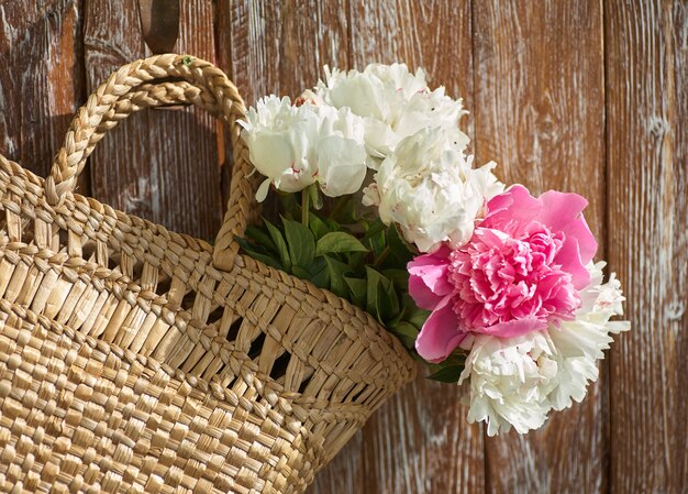 Flores de peonías rosas rojas y blancas en cesta de mimbre en mesa de madera sobre fondo de madera