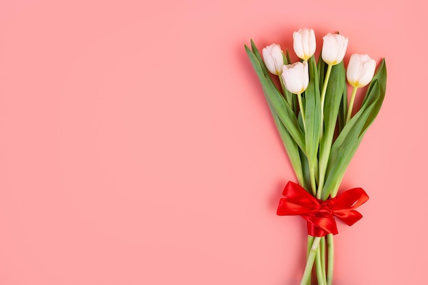 Flores planas Un hermoso ramo atado con una cinta roja y un sobre sobre fondo rosa