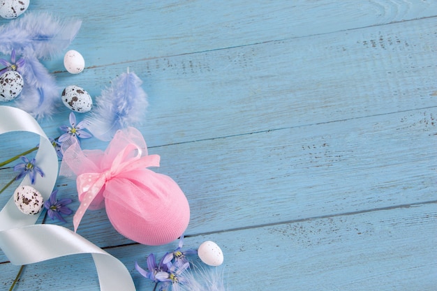 Flores de plantilla-campanilla de Pascua, huevos de Pascua y plumas sobre tablero de madera azul.