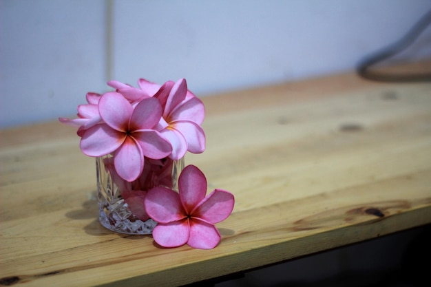 Flores de plumeria rosa en vidrio sobre mesa