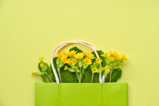 Flores de primavera amarilla en una bolsa de compras verde con espacio para texto en papel amarillo