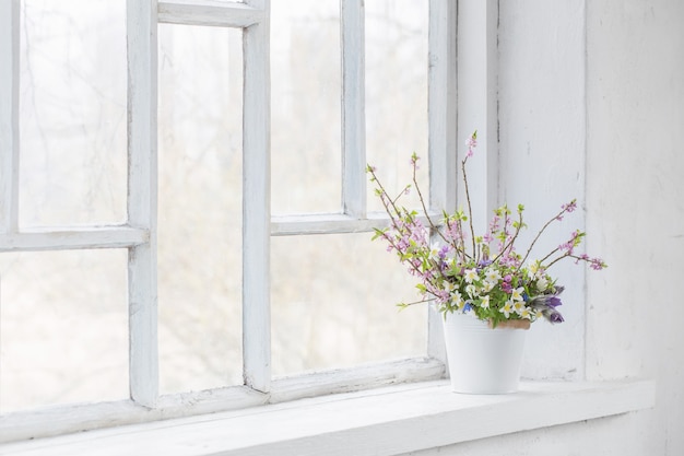 Flores de primavera en balde blanco en el antiguo alféizar blanco