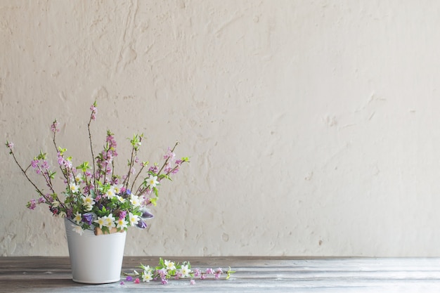 Flores de primavera en balde blanco sobre fondo antiguo muro blanco