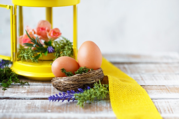 Flores de primavera brillante con huevos de Pascua cerca de una linterna decorativa amarilla