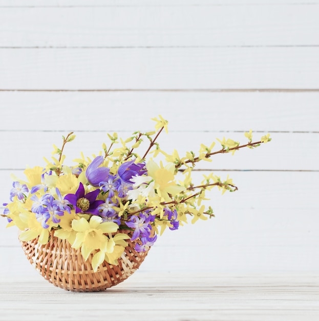 Flores de primavera en canasta sobre superficie de madera blanca