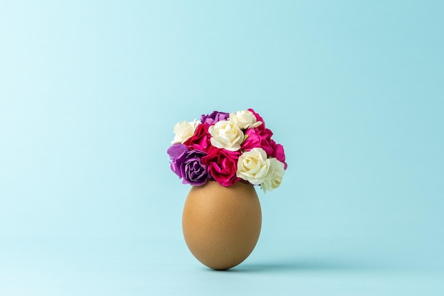 Flores de primavera en cáscara de huevo agrietada contra el fondo azul pastel