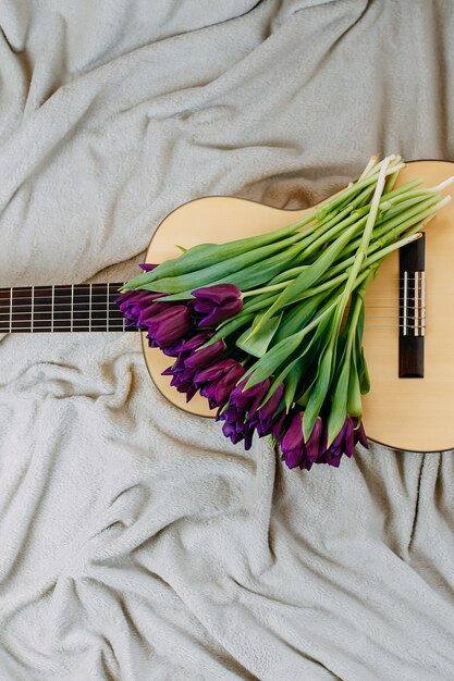 Flores de primavera, tulipanes morados, guitarra blanca y flores sobre fondo gris, póster de música de primavera, ramo de tulipanes morados en la guitarra.