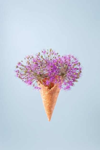 Flores púrpuras redondas en una taza de waffle de un helado sobre un fondo azul. concepto de verano minimalista.