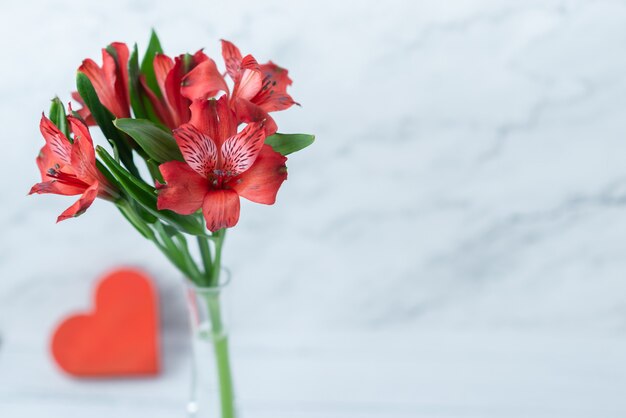 Flores rojas y un corazón rojo sobre un fondo blanco de madera. Tarjeta de felicitación para el 14 de febrero. Primer plano con espacio para texto. Concepto de amor