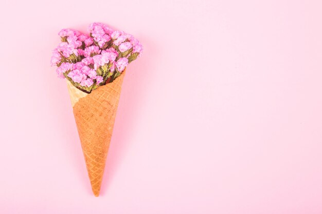 Flores rosadas hermosas en un cono de la galleta para el helado en un fondo rosado brillante.
