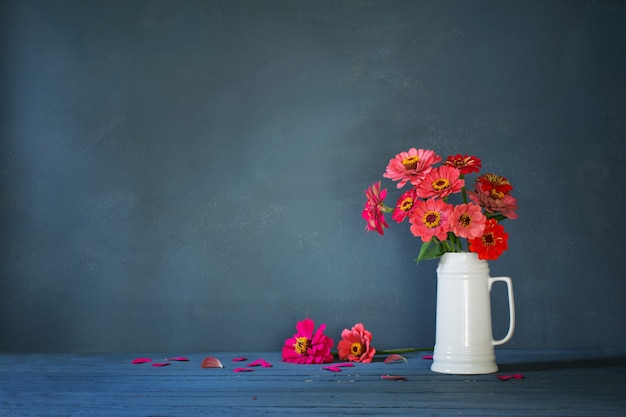 Flores rosadas en jarra blanca sobre fondo azul oscuro