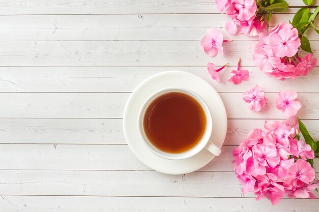 Flores rosadas del Phlox y una taza de café en una tabla blanca.