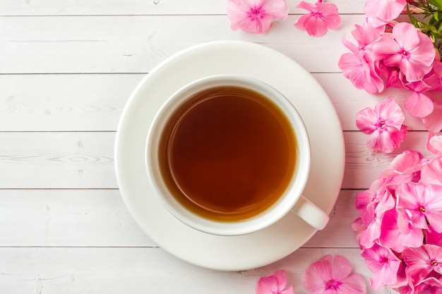 Flores rosadas del polemonio y una taza de café en una tabla blanca.