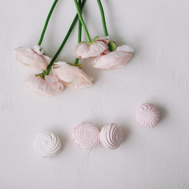 Flores rosas cor de rosa e marshmallows em uma superfície branca